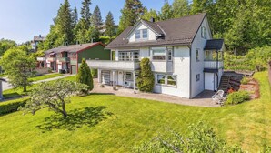 Een huis met twee verdiepingen, een overdekte veranda, een klein terras en een verzorgd gazon.