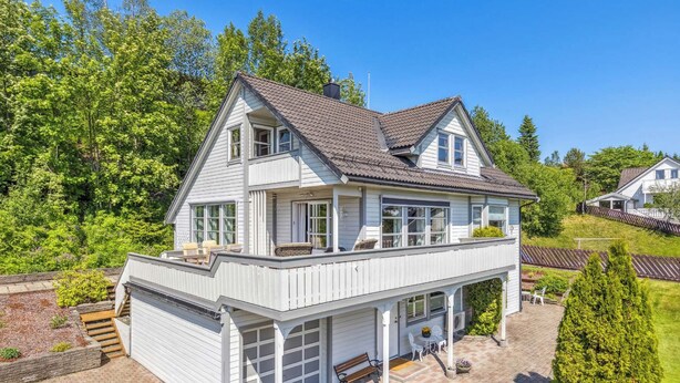 Een tweelaags huis met een grote garage, een balkon met buitenmeubels en een keurig onderhouden tuin.