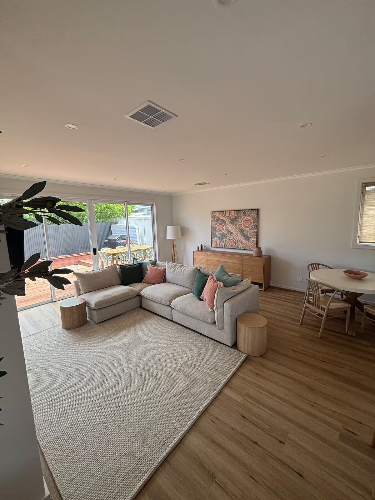 A modern living room with a sectional sofa, a dining table with chairs, and a large window providing a view of the outside.