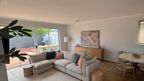 A modern living room with a sectional sofa, a dining table with chairs, and a large window providing a view of the outside.