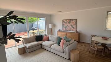 A modern living room with a sectional sofa, a dining table with chairs, and a large window providing a view of the outside.