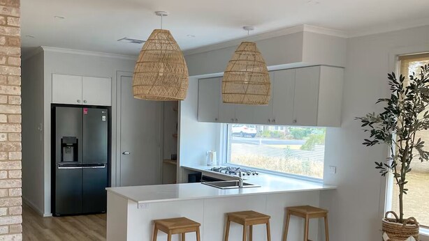 A modern kitchen with white cabinets, a black refrigerator, and a central island with stools.
