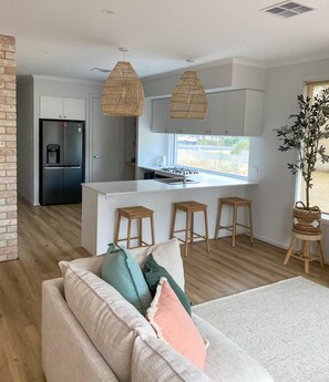 Une cuisine moderne avec des meubles blancs, un réfrigérateur noir et un îlot central doté de tabourets.