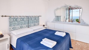 A bedroom with a bed, a nightstand with a lamp, a mirror, and a window with a view.