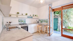 A modern kitchen with a built-in stove, microwave, and sink. There are two wooden stools and a window with a view of greenery outside.