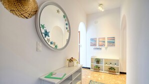 A hallway with a round mirror, a white console table, and a shelf with plants.