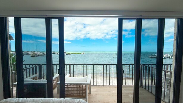 A room with a large sliding glass door leading to a balcony with a view of the sea and marina.