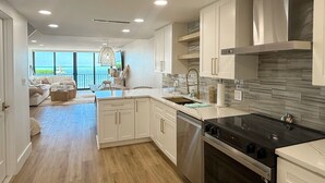 A modern kitchen with white cabinetry, a black stove, and a view of the ocean through large windows.