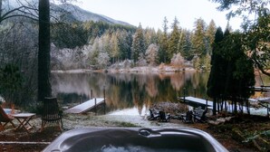 Un bain à remous avec vue sur un lac, entouré d’arbres et doté d’un quai.