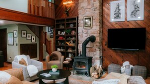Un salon chaleureux avec une cheminée, des fauteuils confortables, une bibliothèque et un téléviseur à écran plat fixé au mur.