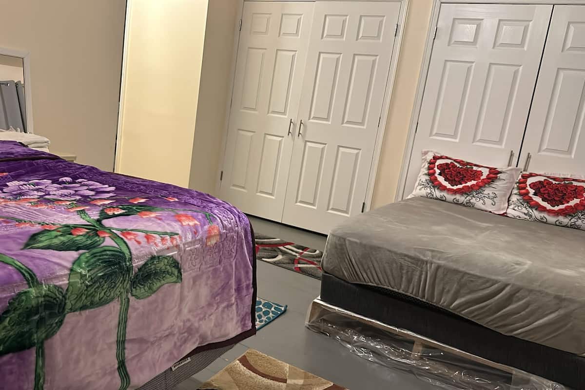 Ein Schlafzimmer mit einem violetten floralen Bettbezug, einer grauen Matratze und einer weißen Tür mit einem Spiegel darüber.