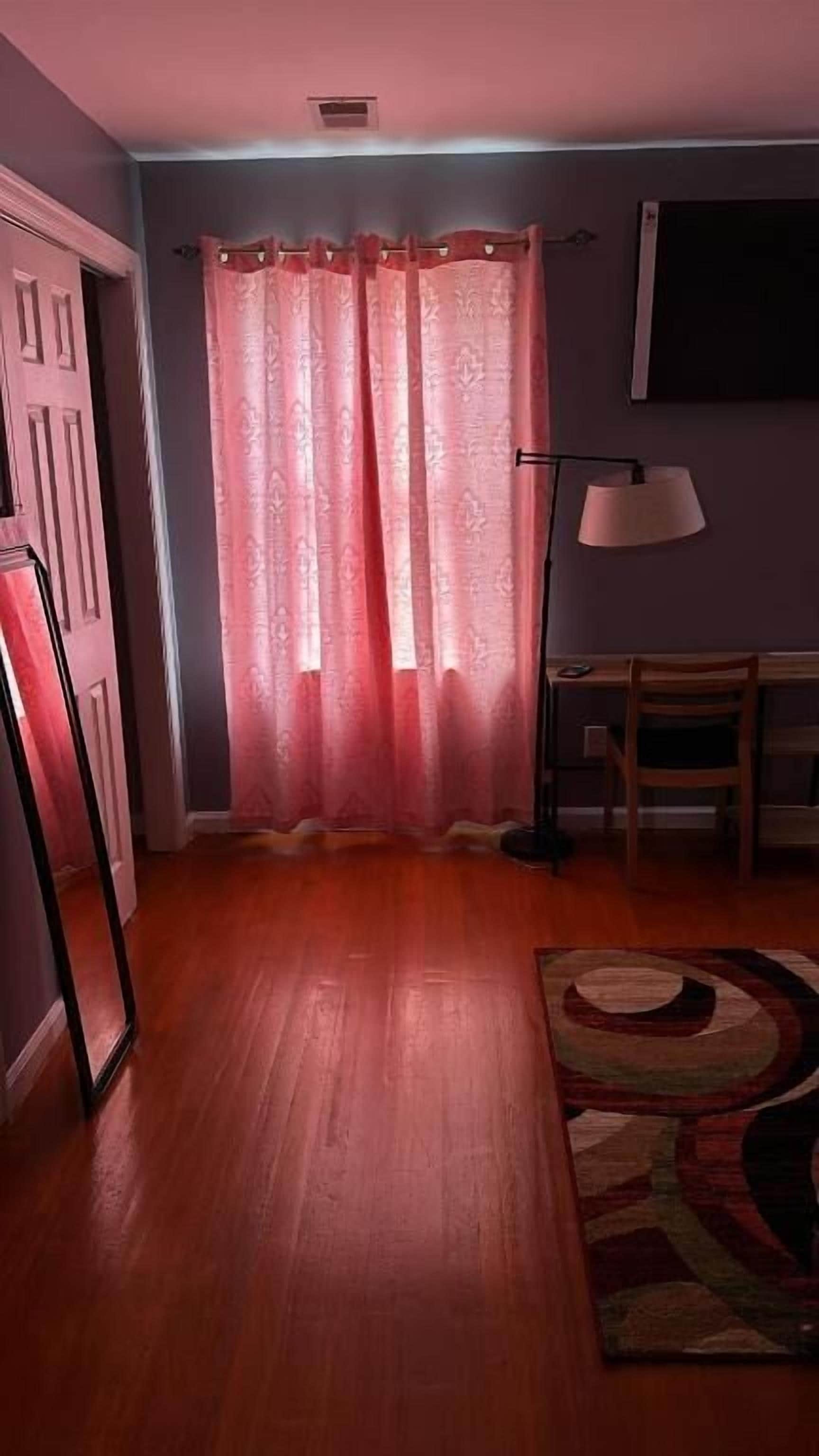 A room with a wooden floor, a pink curtain, a desk, and a chair.