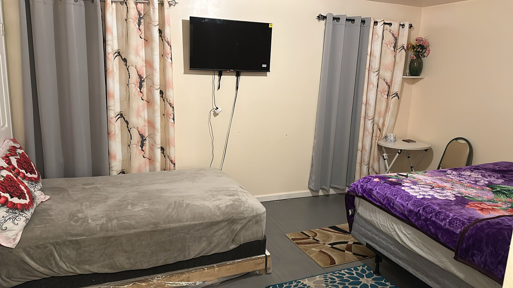 A bedroom with two beds, a TV mounted on the wall, and a small table with a vase of flowers.