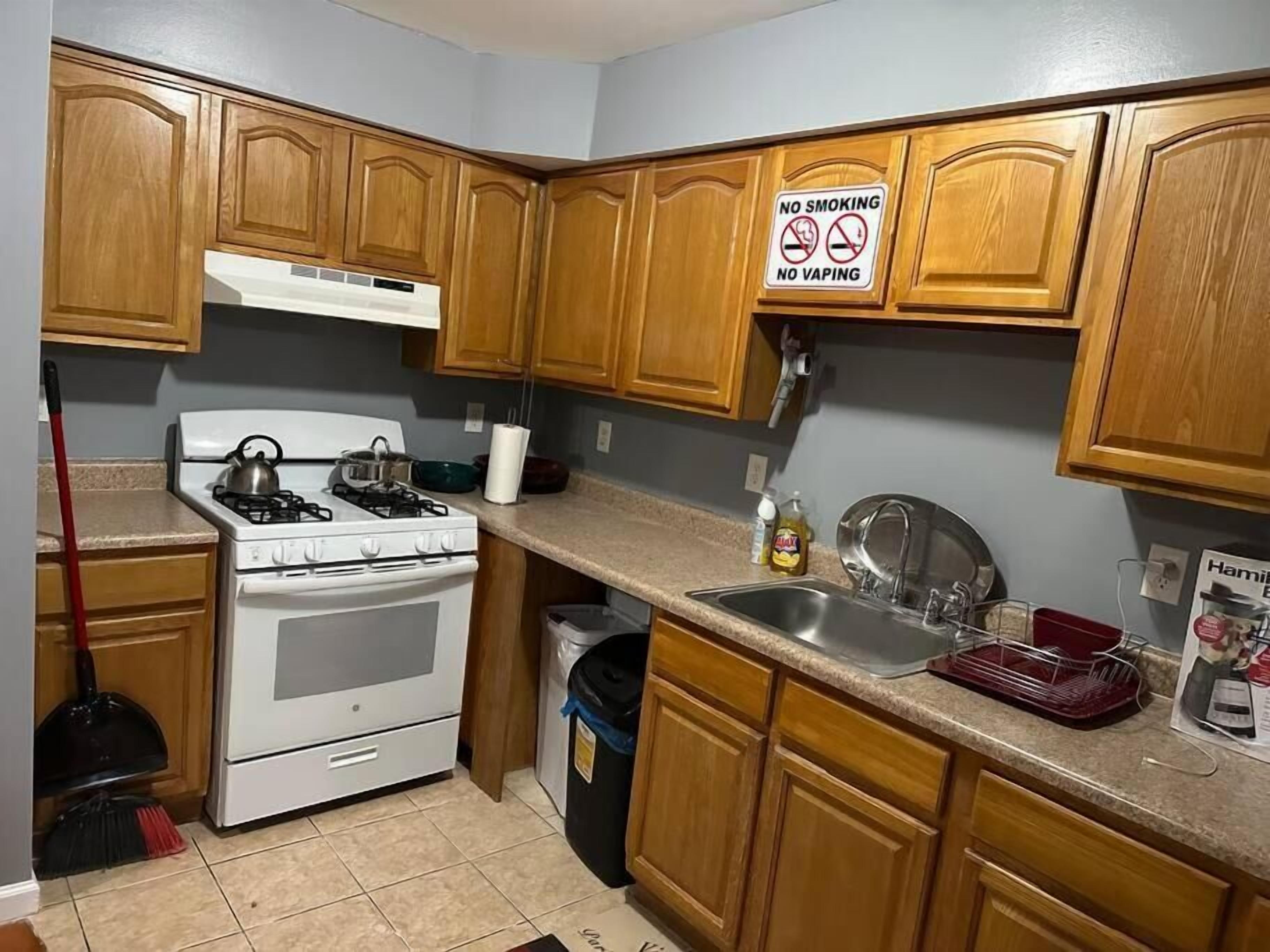 A kitchen with wooden cabinets, a stove, a sink, and a trash bin.