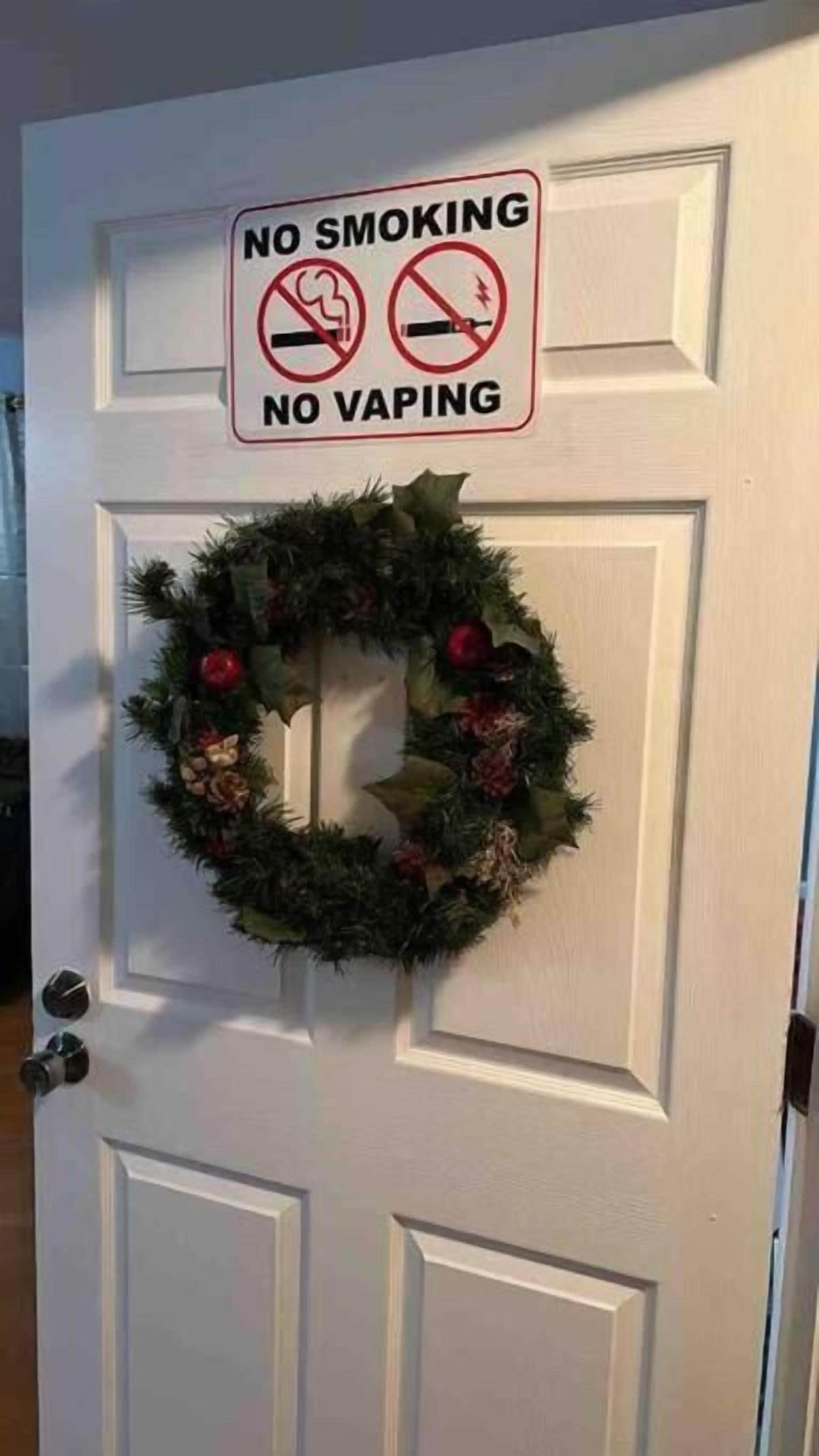 A door with a 'No Smoking' and 'No Vaping' sign above a Christmas wreath.