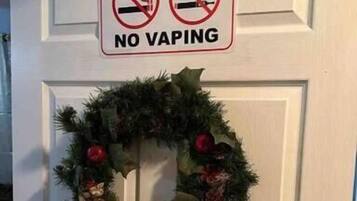 Puerta con un letrero de 'No Fumar' y 'No Vaping' sobre un adorno navideño.