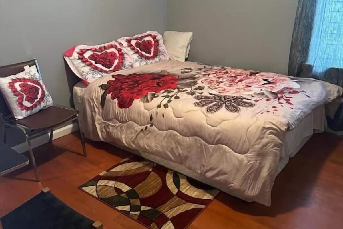 Ein Schlafzimmer mit einem Bett, einem Sessel, einem kleinen Tisch und einem gemusterten Teppich.