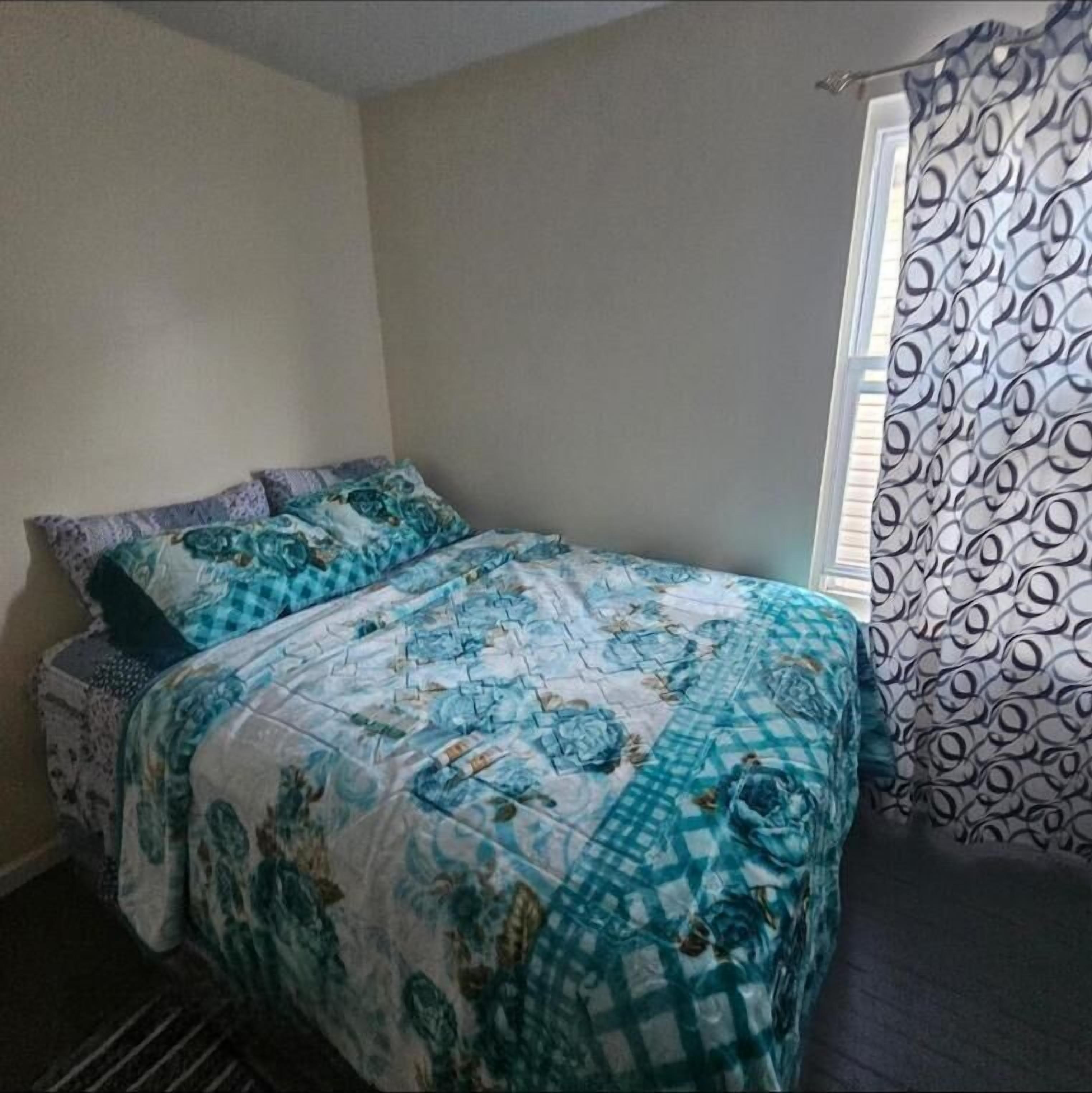 Une chambre à coucher avec un lit, une fenêtre ornée de rideaux à motifs et un mur uni.