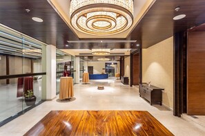 Un moderno vestíbulo de hotel con piso de madera pulida, un mostrador de recepción y una gran lámpara de araña circular.