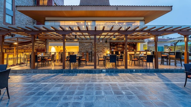 An outdoor patio area with tables and chairs, a stone wall, and a covered seating area. - Ramada by Wyndham Kathmandu Dhumbarahi (Kathmandu)