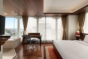 Habitación de hotel con cama, escritorio con silla, televisor y vista a la ciudad.