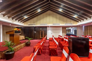 A conference room with rows of red chairs, a podium, and a stage. - Ramada by Wyndham Kathmandu Dhumbarahi (Kathmandu)