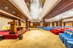 Un salón de conferencias con un escenario, filas de sillas y una gran lámpara de cristal.
