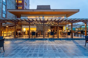 Un patio al aire libre con mesas y sillas, un muro de piedra y una zona de estar cubierta.