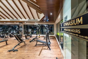 A gymnasium with exercise equipment, wooden flooring, and a sign detailing operation hours. - Ramada by Wyndham Kathmandu Dhumbarahi (Kathmandu)