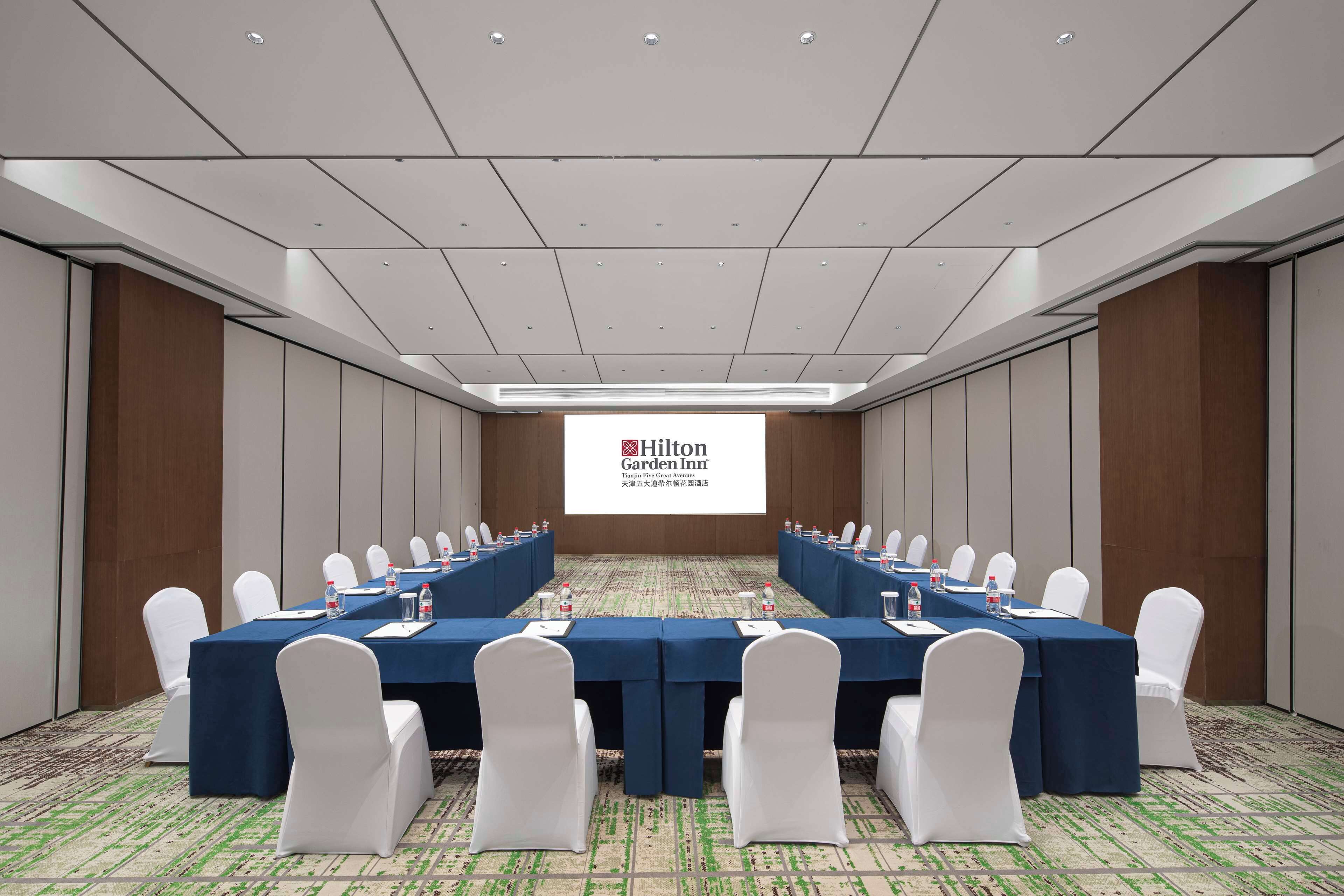 A conference room with a long table, white chairs, and a Hilton Garden Inn logo on the screen.