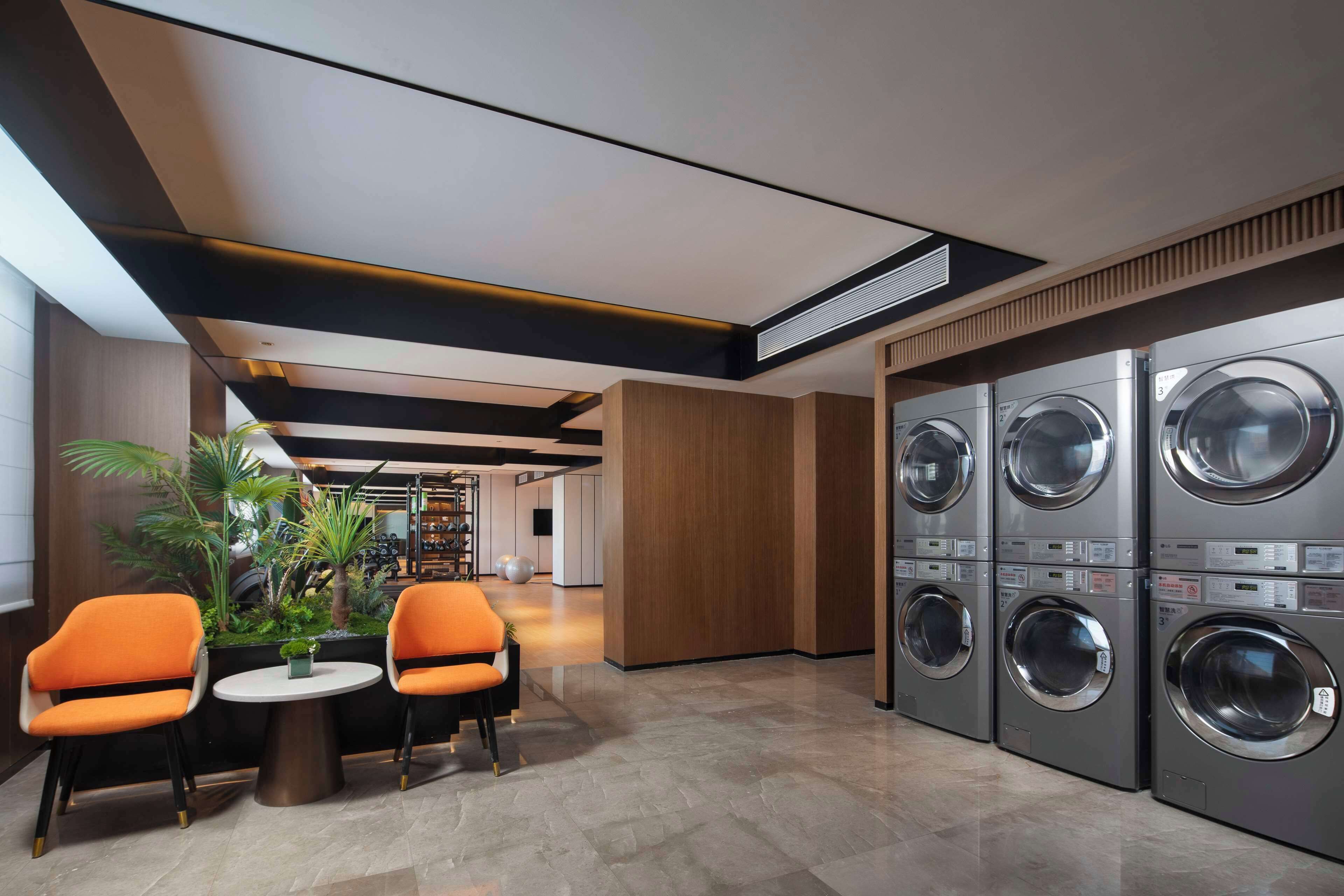 Een moderne hotel lobby met een zithoek, een plant en een rij wasmachines.