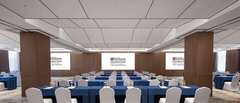 A conference room with multiple tables, white chairs, and a large screen displaying the Hilton Garden Inn logo.