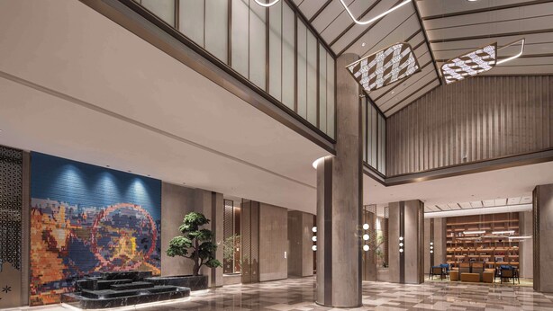Un hall amplio con piso a cuadros, un gran mural abstracto y una zona de estar con mesas y sillas.