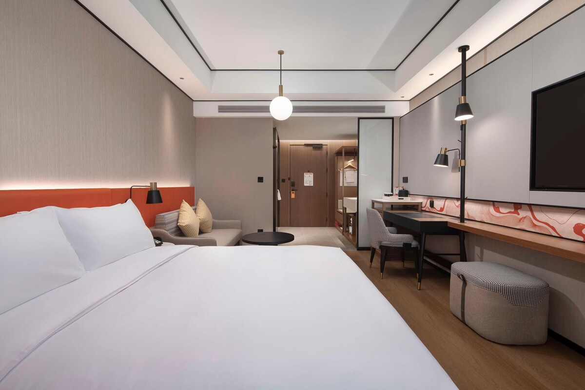 Una habitación de hotel moderna con una cama grande, un escritorio, una silla y un pequeño reposapiés.