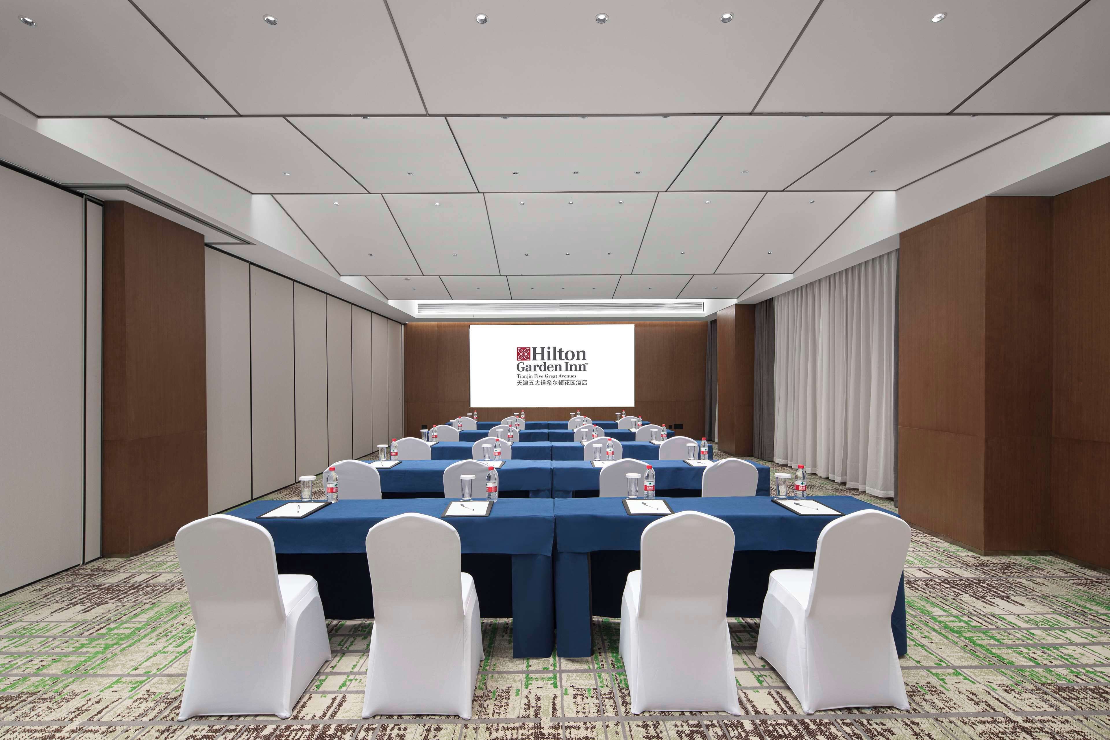 A conference room with a long table, white chairs, and a presentation screen displaying 'Hilton Garden Inn'.