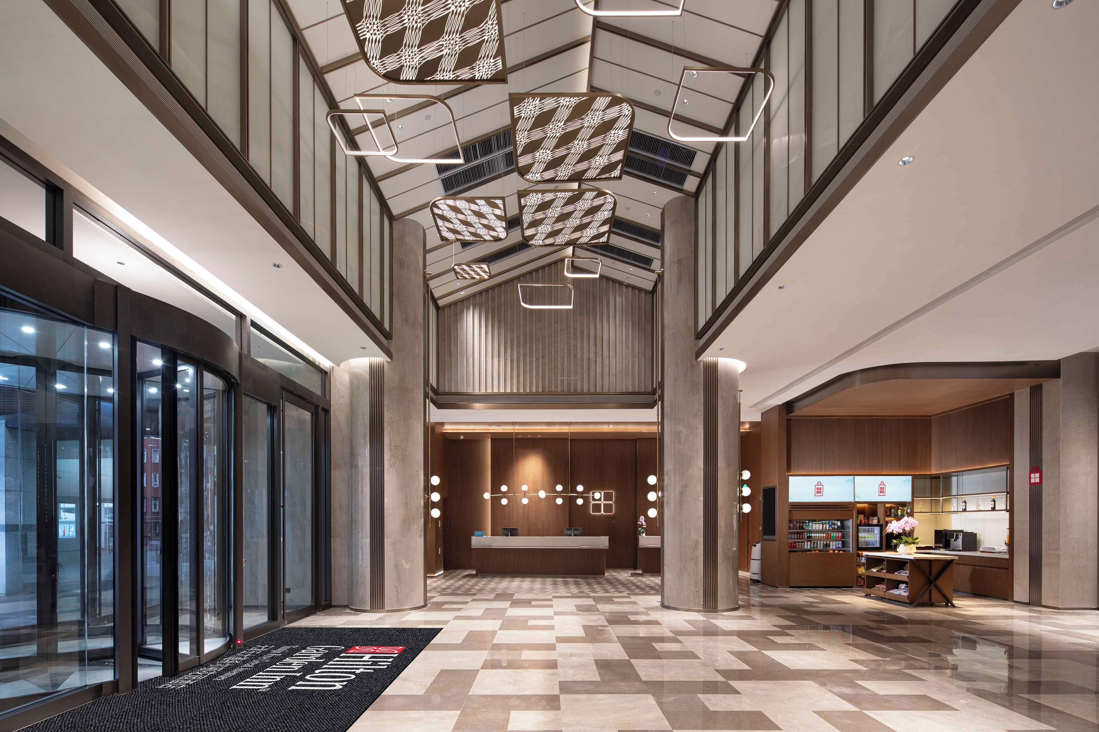 A modern hotel lobby with a reception desk, a coffee shop, and a check-in area.