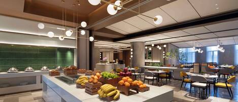 A modern hotel lobby with a central buffet area, seating arrangements, and a large window providing natural light.