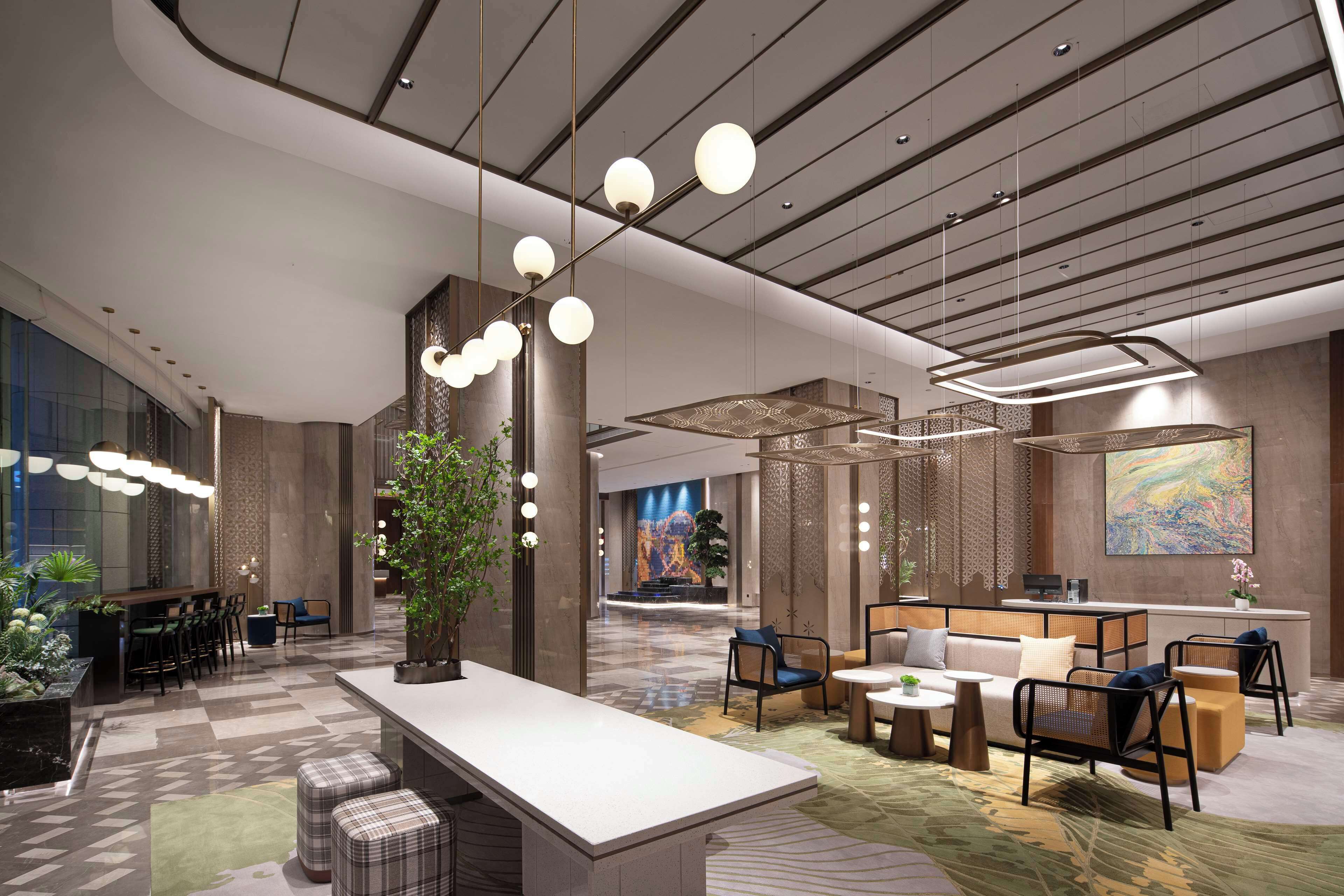 A modern hotel lobby with a reception desk, seating areas, and a large abstract painting on the wall.