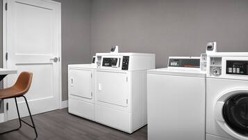 A laundry room with two front-loading washing machines and a dryer, a white door, and a brown chair.