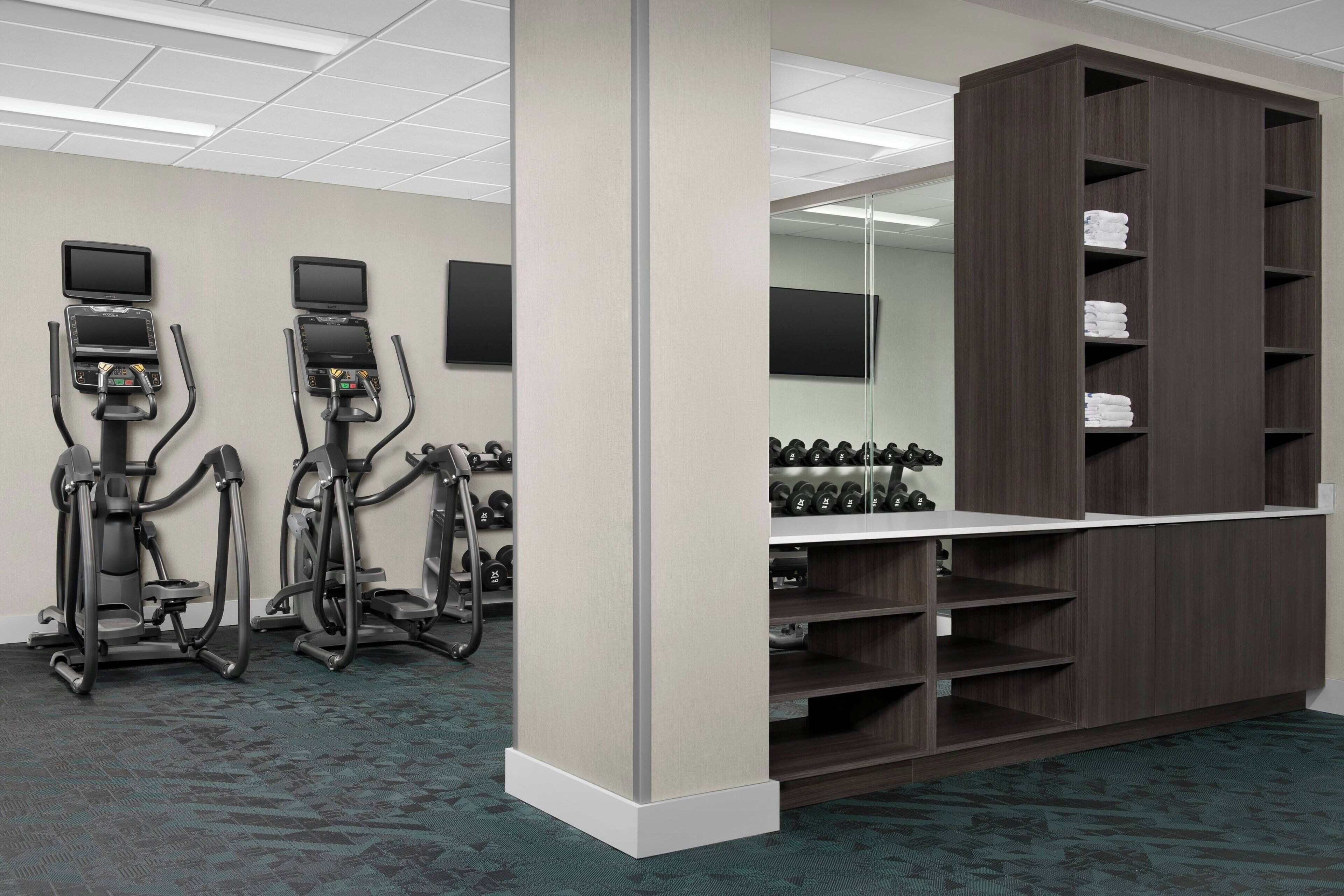 A gym with treadmills, weight machines, and a wall-mounted TV.