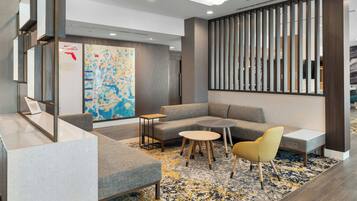 A modern lounge area with a sectional sofa, round tables, and a yellow chair. A large abstract painting and a map are on the wall.