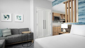 Una habitación de hotel con cama, sofá, una mesita, armario y kitchenette.