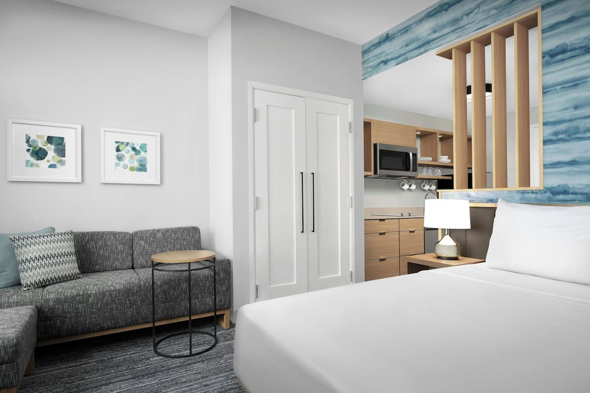 A hotel room with a bed, a sofa, a small table, a wardrobe, and a kitchenette.