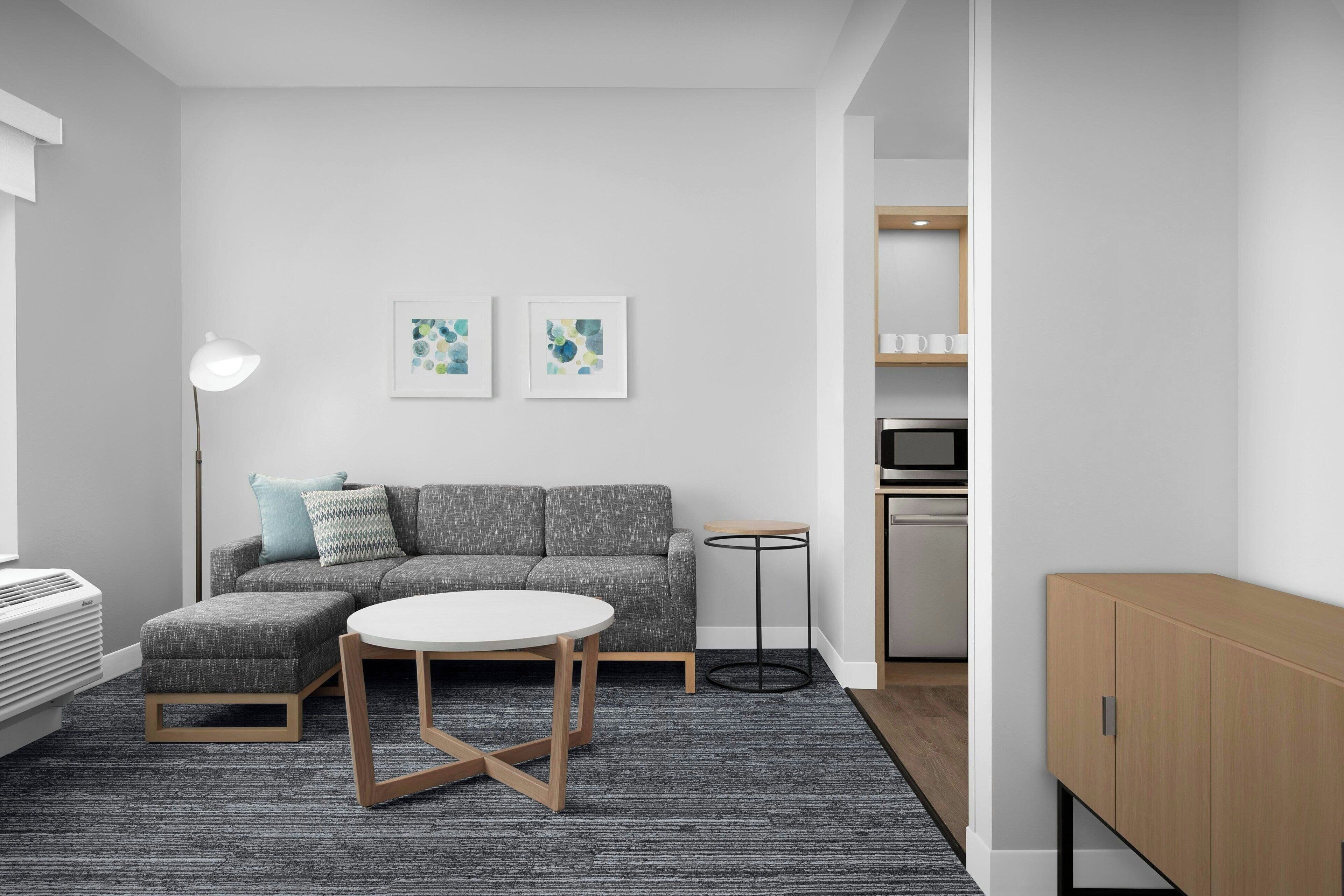 A modern living room with a grey sofa, a round table, a floor lamp, and two abstract art pieces on the wall.
