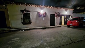 A building with a tiled roof, a door, and a parked red car. - San Carlos I House (Antigua Guatemala)