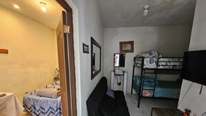 A compact room with a bunk bed, a small desk, a chair, a bedside table, a mirror, and a wall-mounted TV. - San Carlos I House (Antigua Guatemala)
