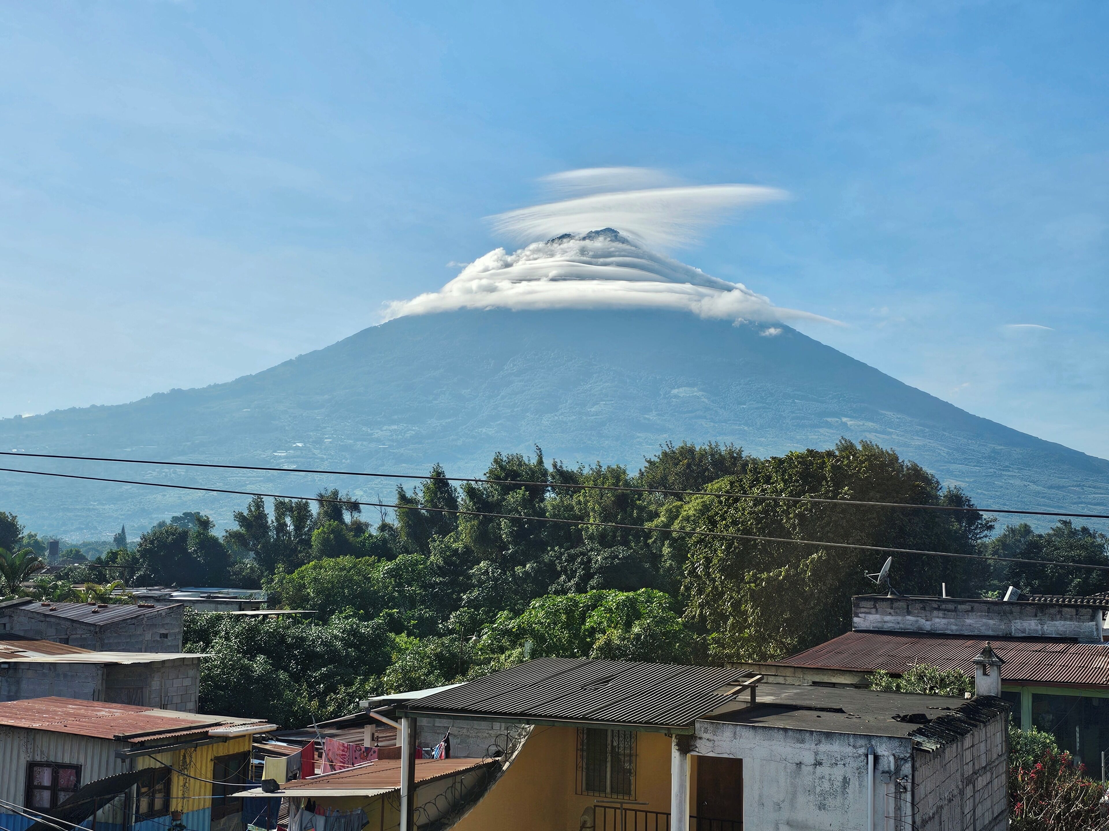 A mountain with a cloud formation at its peak, surrounded by residential buildings and greenery.