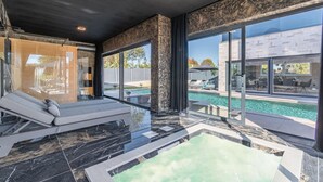 A modern indoor pool area with a lounge chair, a hot tub, and large windows offering a view of the outside. - Jacuzzi and Sauna Villa (Labin)