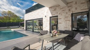 A modern outdoor patio with a pool, seating area, and a dining table. - Jacuzzi and Sauna Villa (Labin)