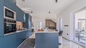 A modern kitchen with built-in appliances, a central island, and a dining area with a view. - Jacuzzi and Sauna Villa (Labin)